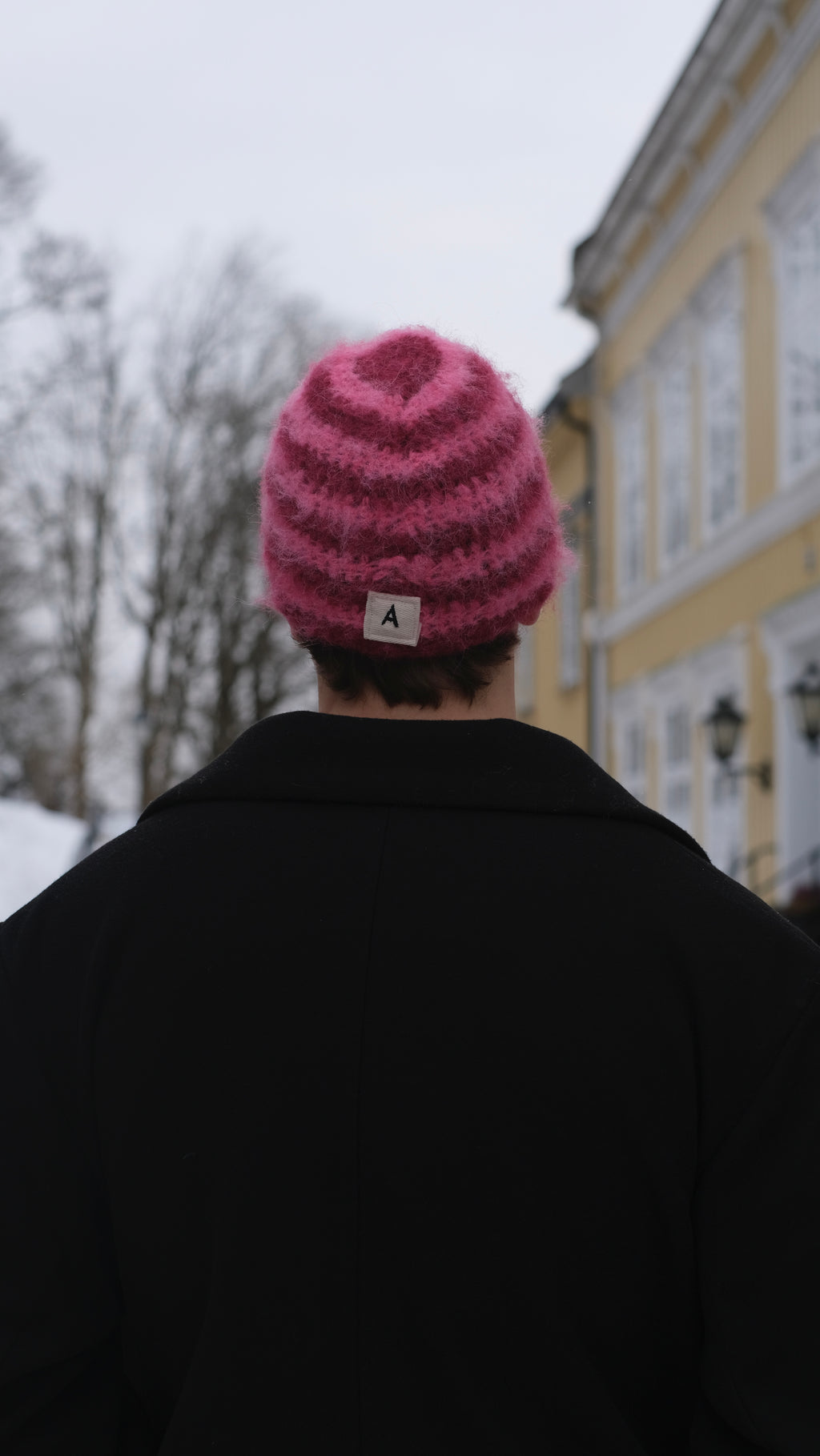 Person wearing a pink knitted beanie with a logo, standing outdoors.