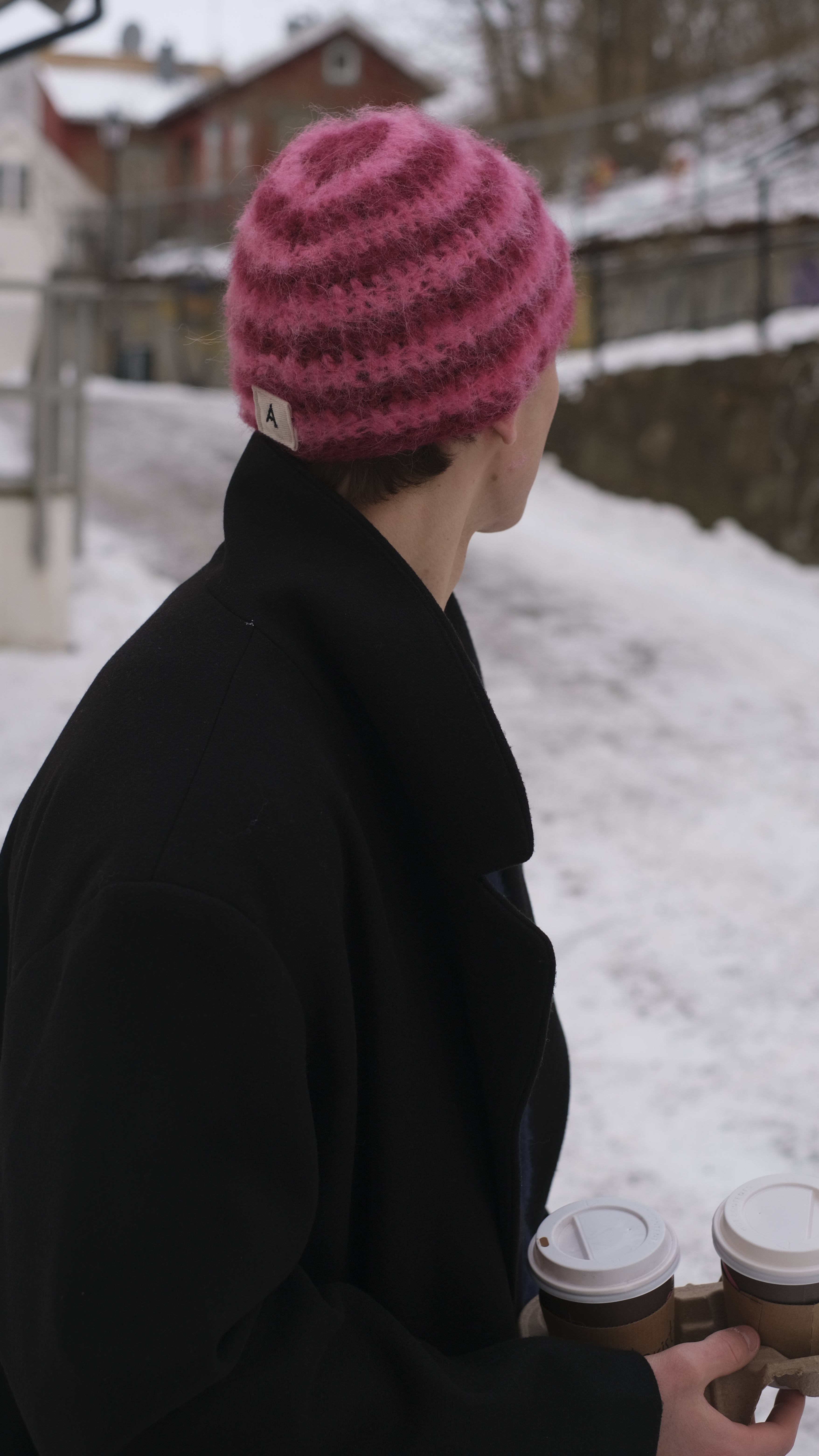 Person wearing a black coat and pink knit hat in a snowy outdoor setting
