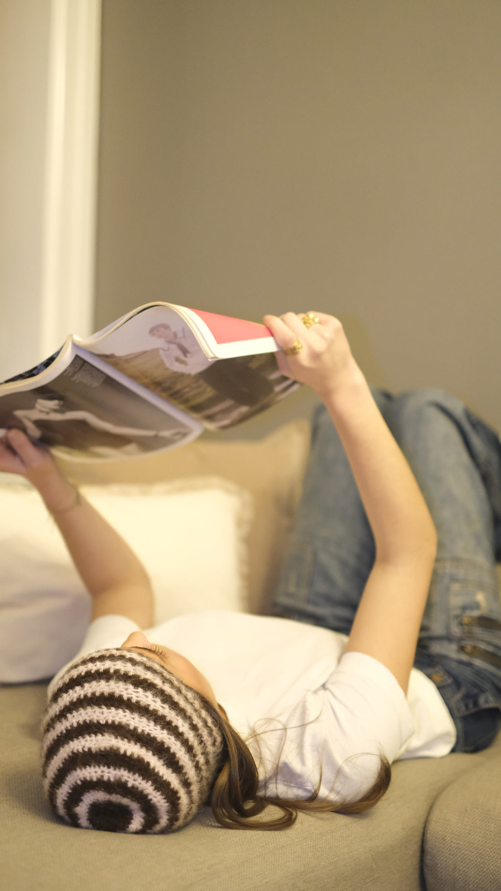 Person wearing a striped beanie and holding a magazine indoors